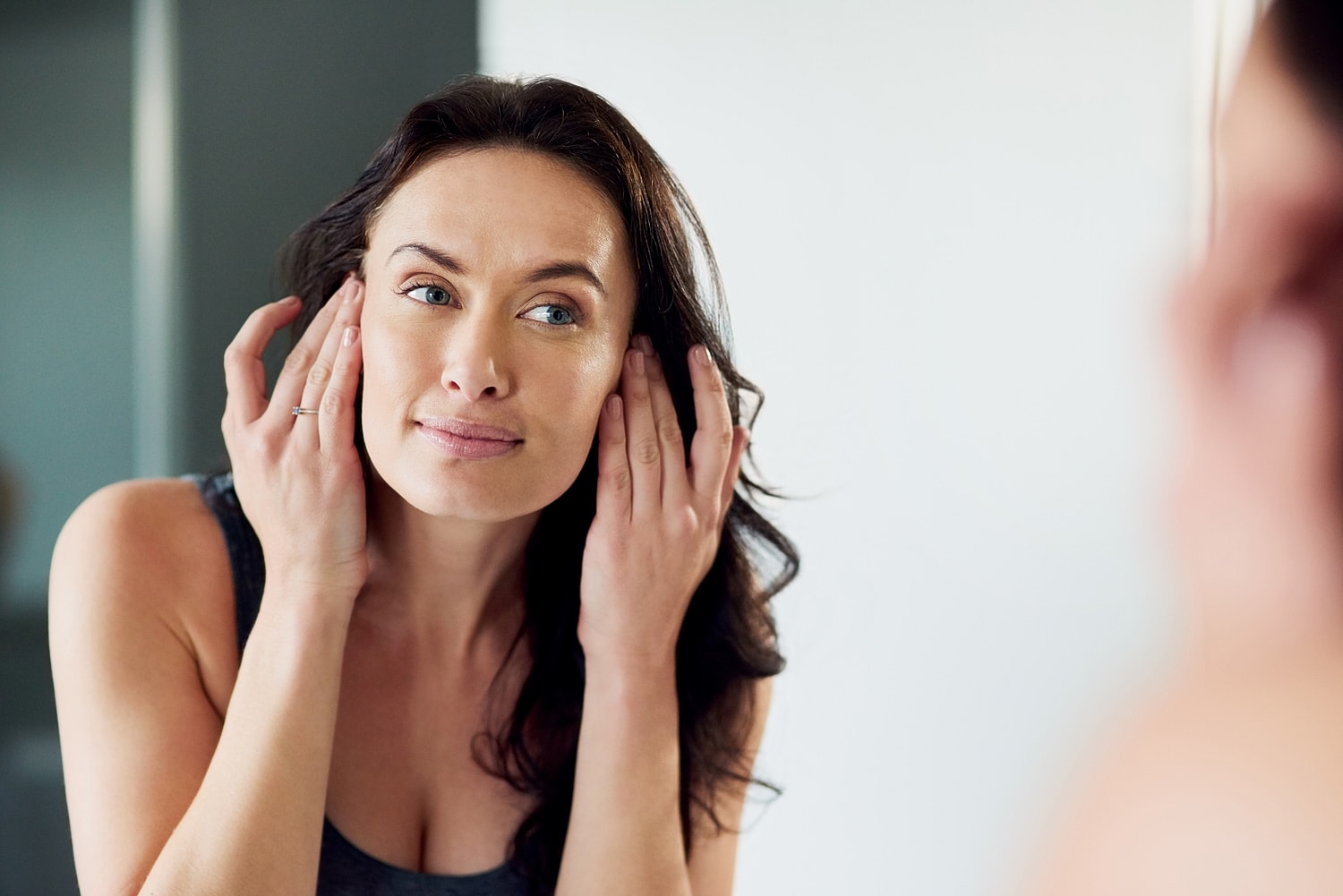 Woman applying skincare in front of a mirror.