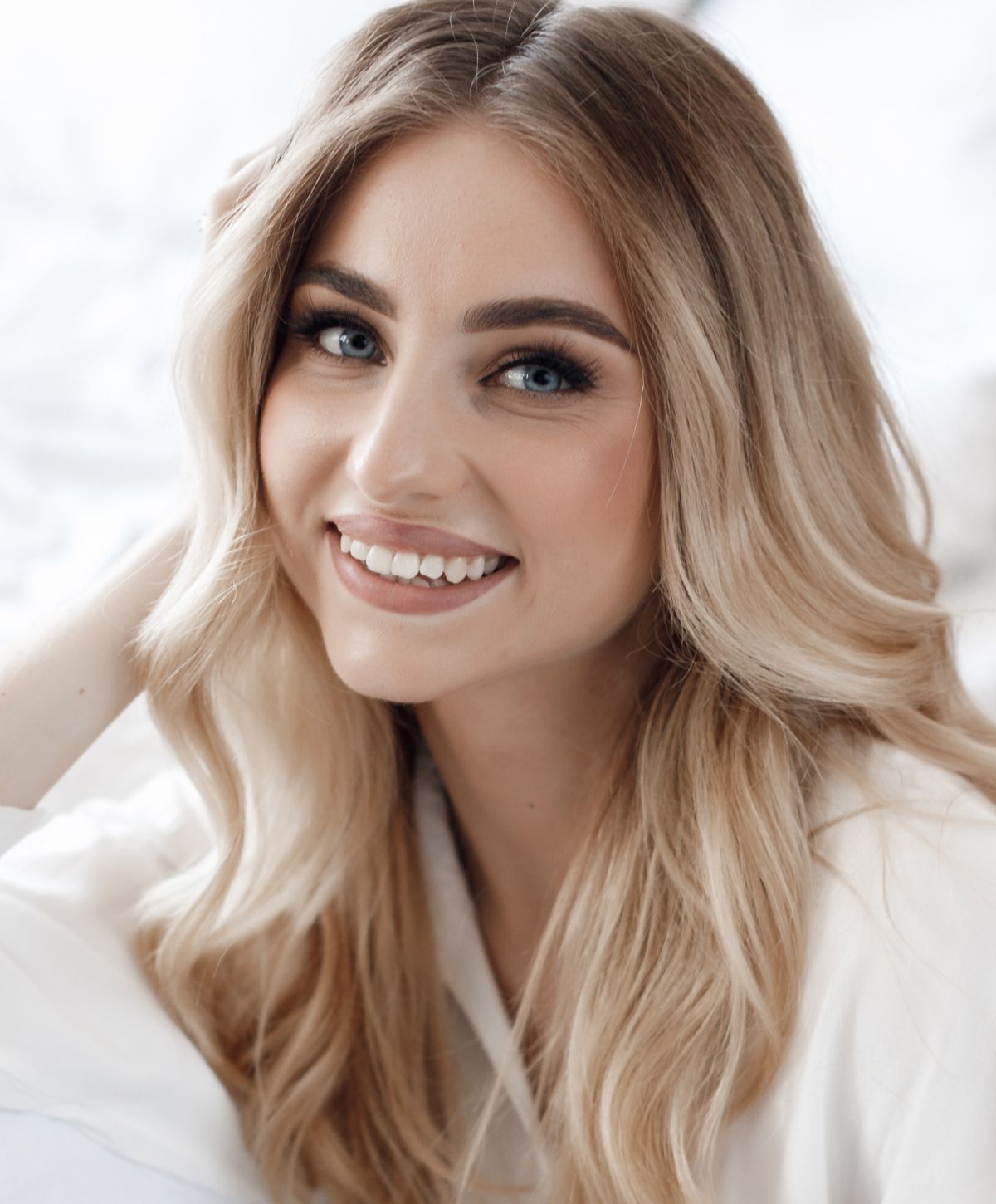 Smiling Newport Beach eyelid lift model with long, wavy blonde hair.