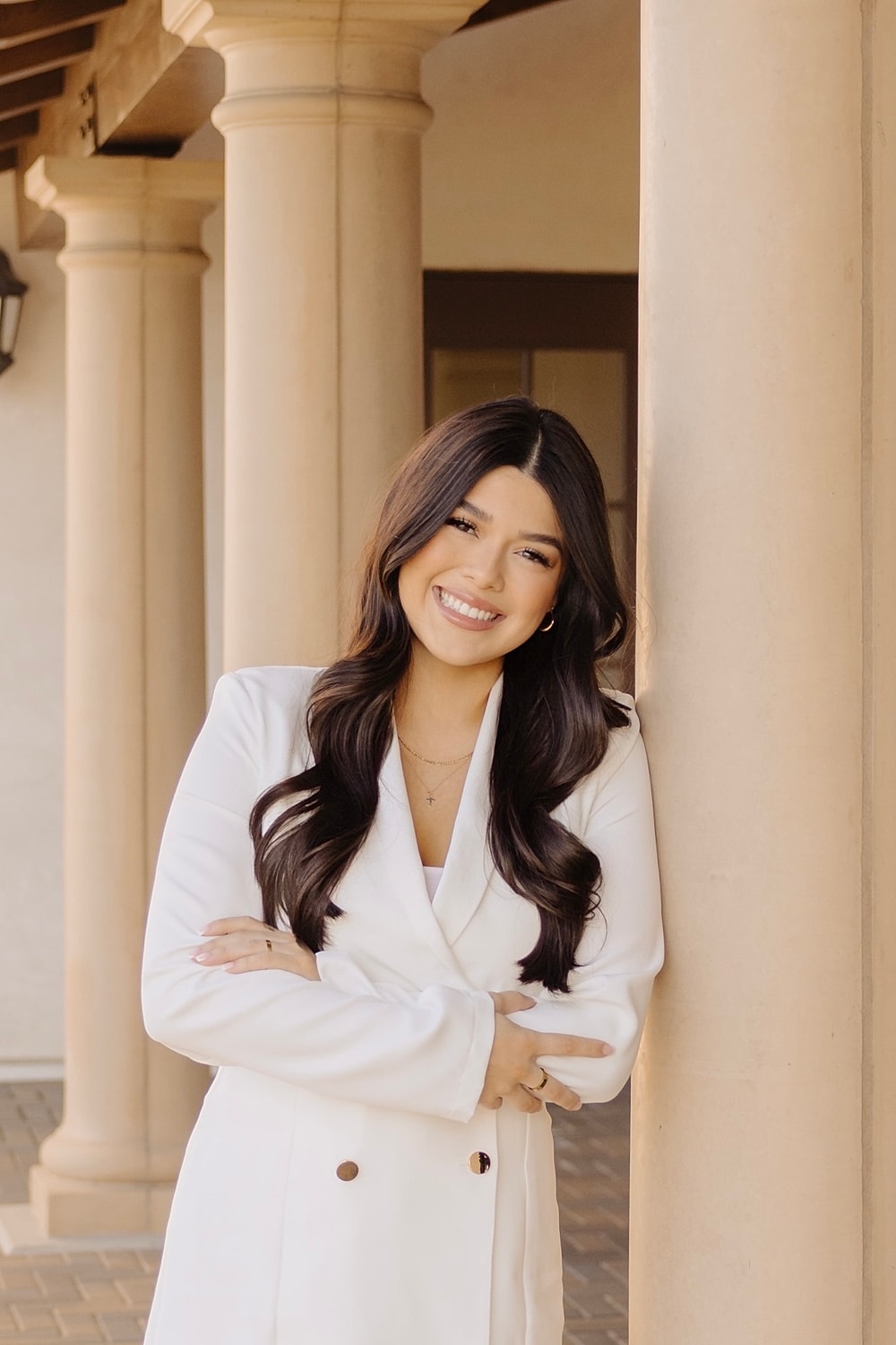 Smiling woman in white coat by pillars.