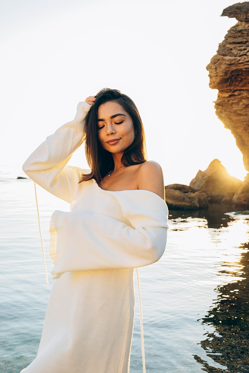 Woman in white dress by the ocean at sunset.
