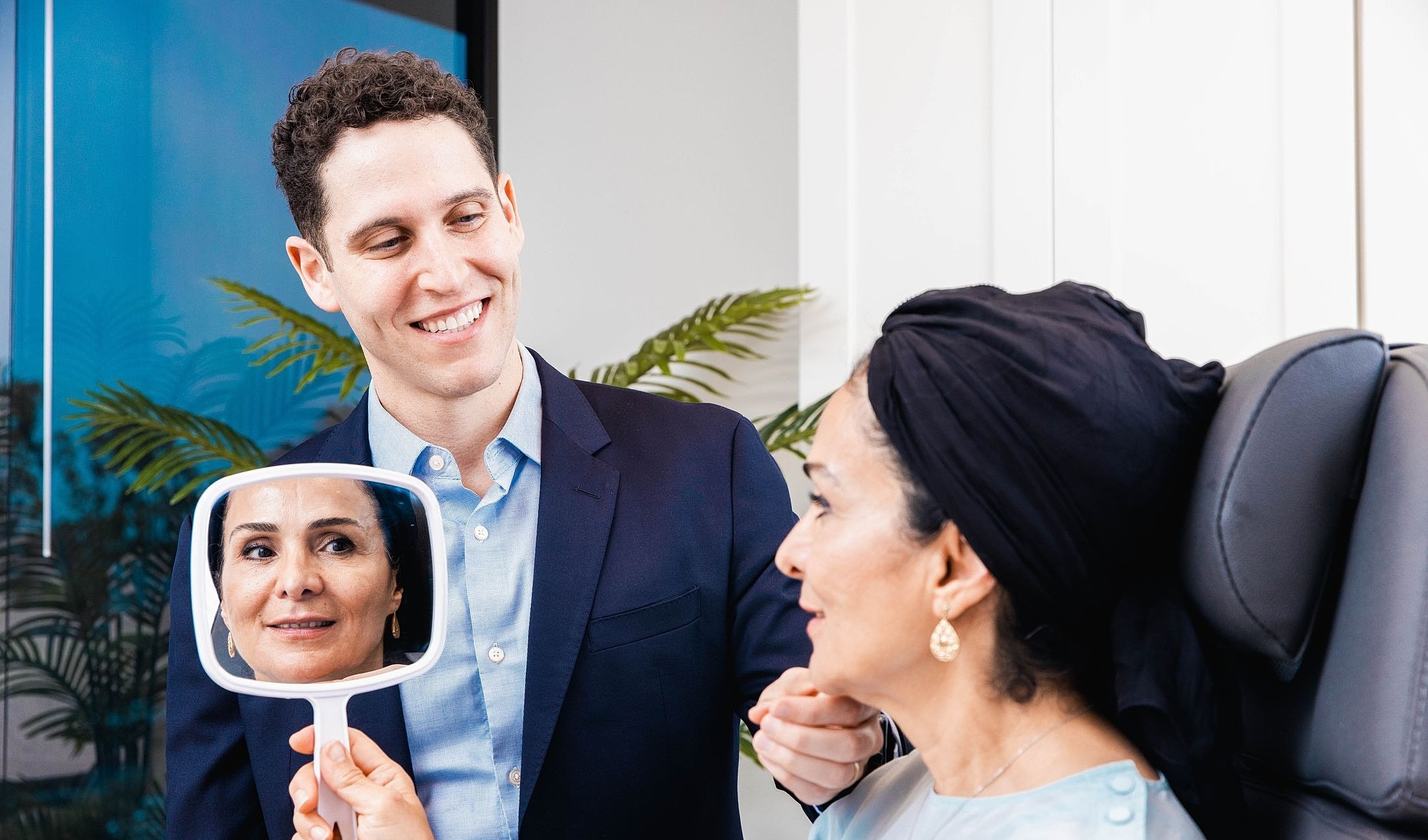 Patient admiring results in mirror with doctor.