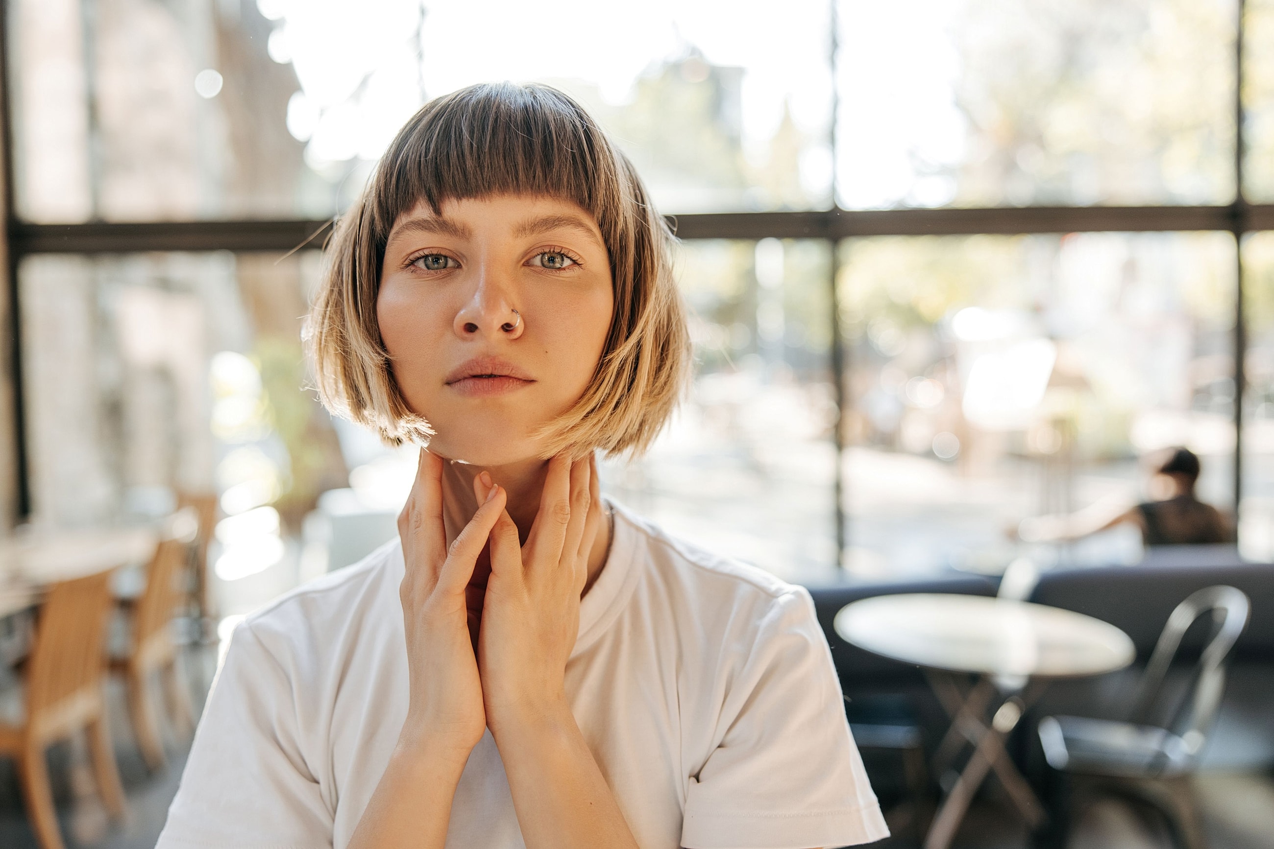Woman touching her neck and jawline while looking in a mirror to check for skin laxity and early signs of aging.