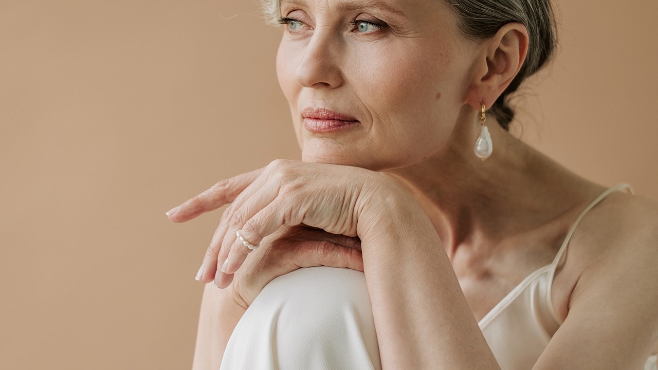 Thoughtful woman in elegant attire against neutral background.