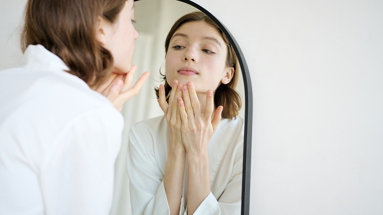 Woman applying skincare in front of a mirror.